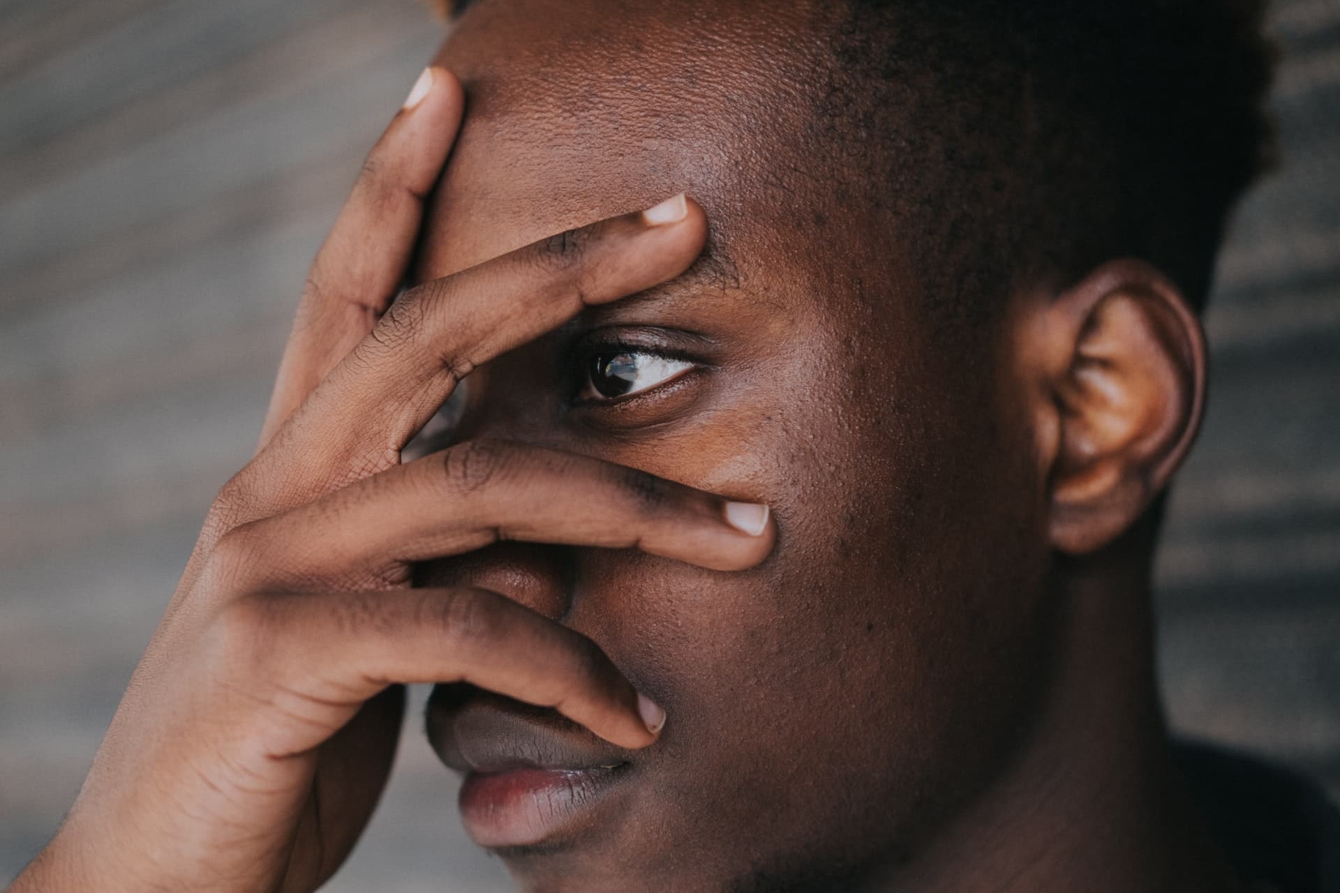 A young man peers anxiously through the fingers of a hand covering his face