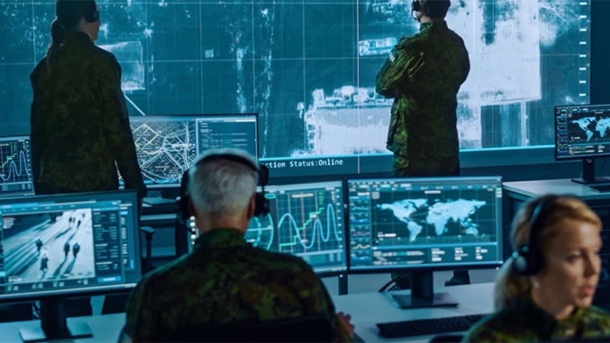 Military personnel monitoring a command-centre wall of live maps, radar feeds and analytics screens
