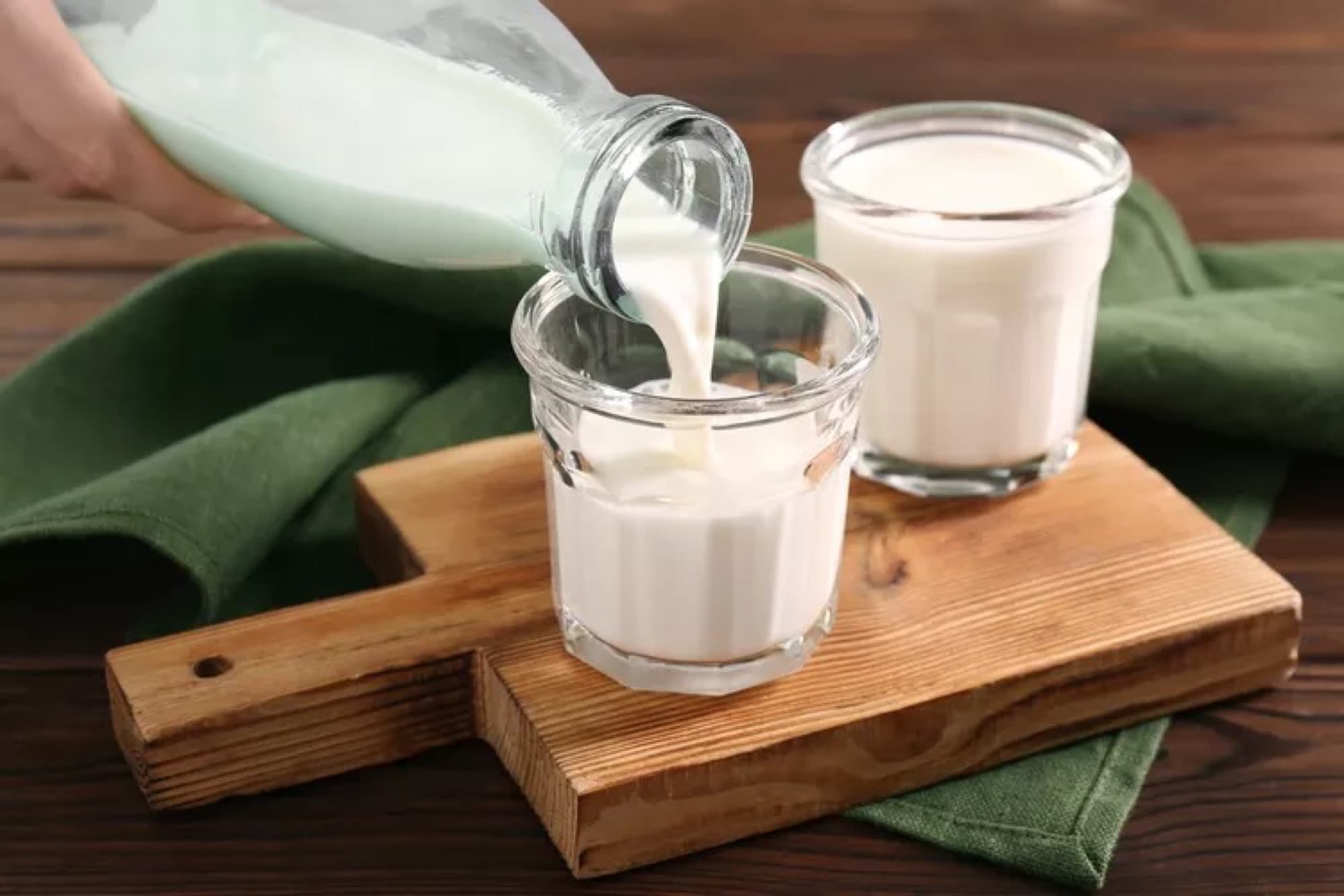 Milk being poured from a bottle into a glass on a wooden board