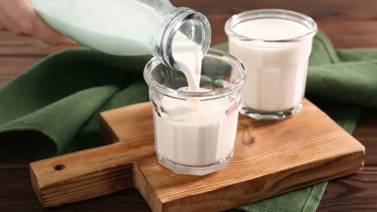 Milk being poured from a bottle into a glass on a wooden board