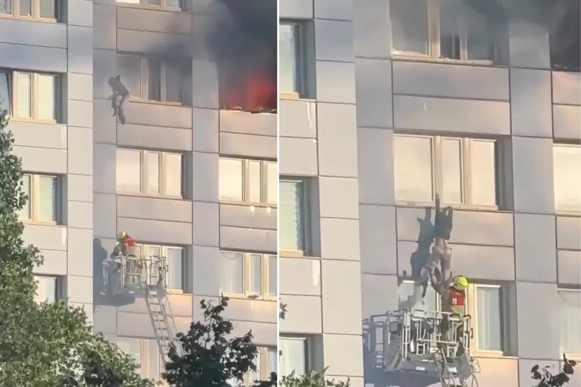 A woman climbs along an 11th floor window ledge of a burning Berlin high rise as a firefighter waits in a rescue basket below