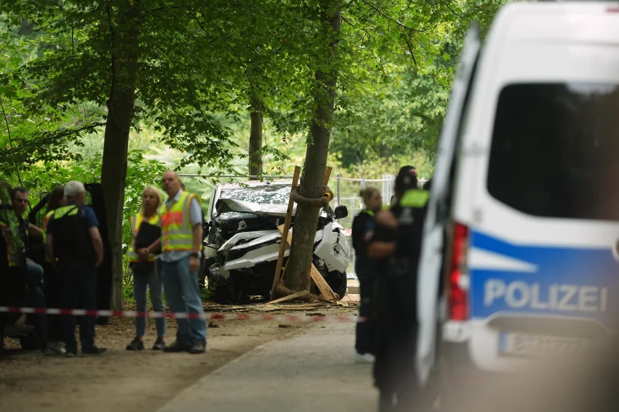 Police and investigators beside a wrecked car pushed against a tree in a Berlin park, cordoned off with tape