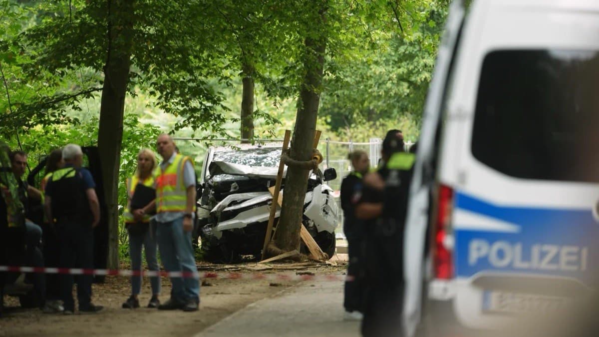Police and investigators beside a wrecked car pushed against a tree in a Berlin park, cordoned off with tape