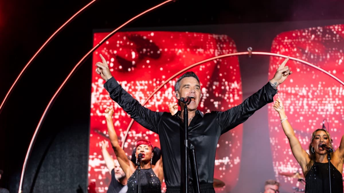 Robbie Williams performing on stage with arms outstretched at BIG ART Festival in Porto Cervo