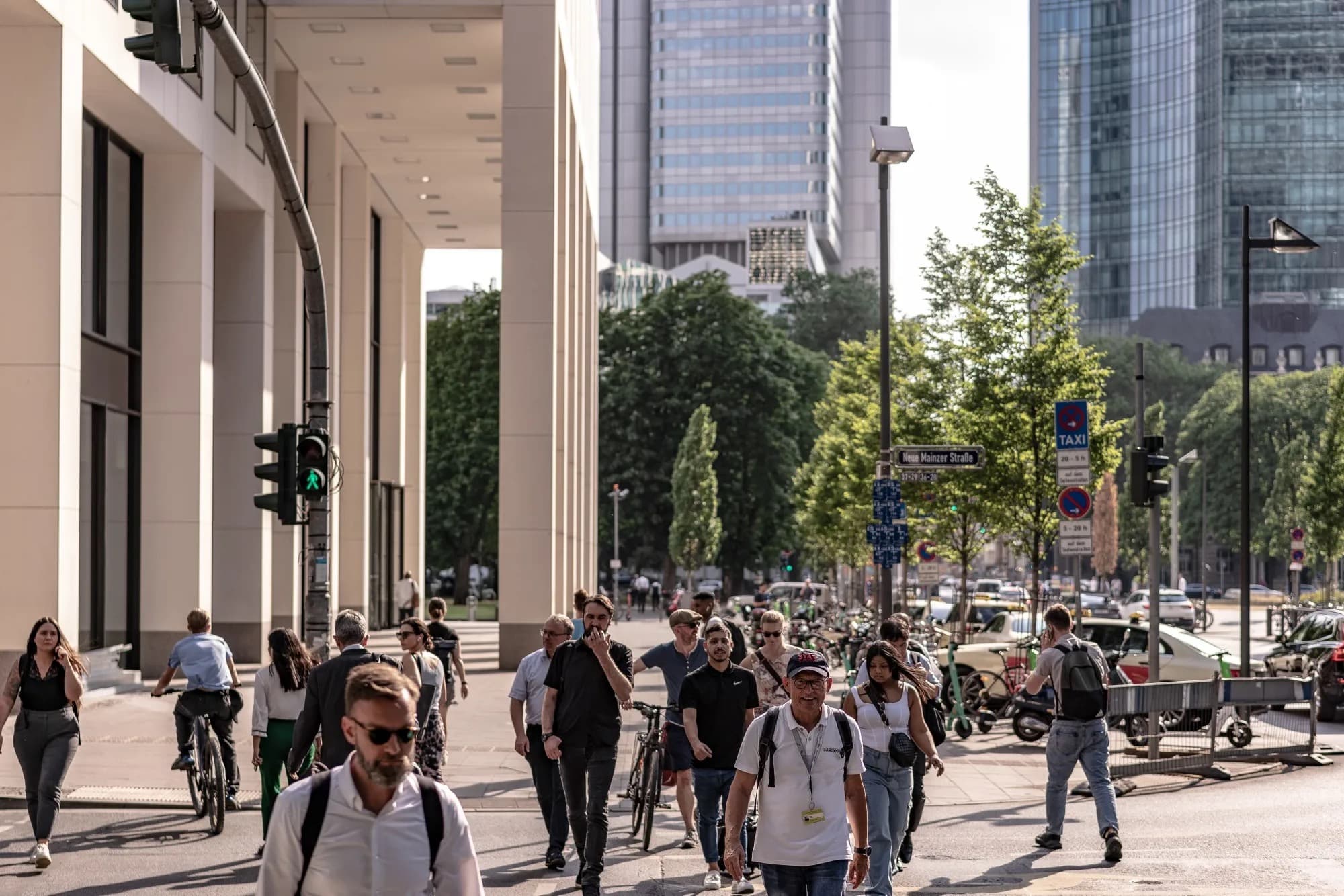 Pedestrians walk past office towers in Frankfurt's financial district on a sunny day