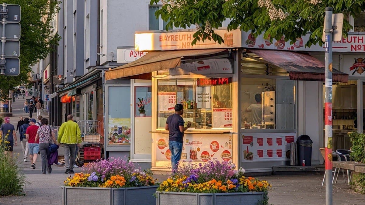 A customer orders at a doner kebab stand on a German street at dusk