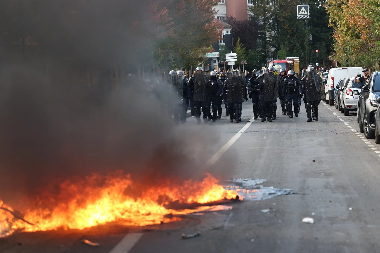 French riot police walking down a smoke-filled street past a burning barricade during cost-of-living protests