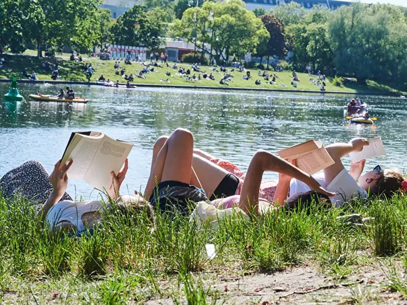 People relaxing and reading by a lake in a Berlin park during the summer heat