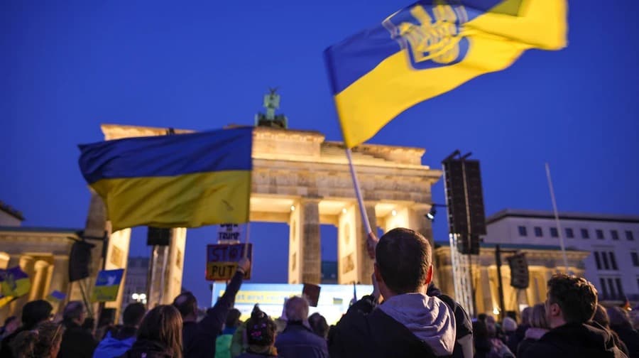 Demonstrators wave Ukrainian flags in front of the Brandenburg Gate in Berlin at dusk