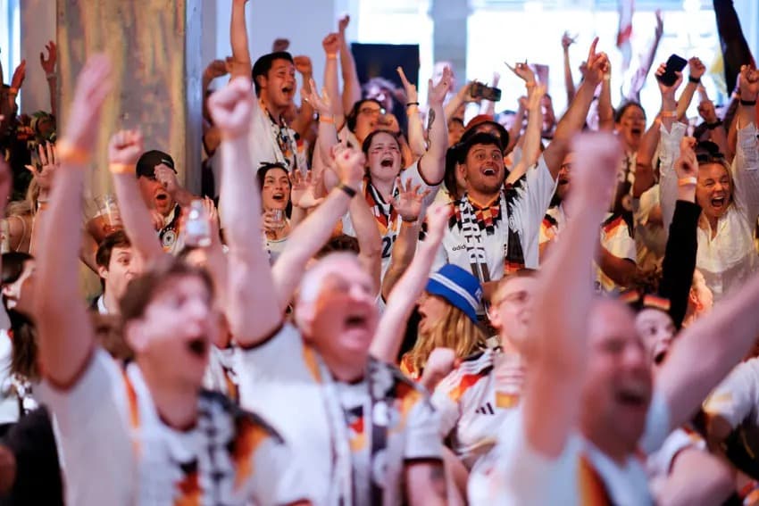 Germany supporters in national team shirts cheer with arms raised at a public viewing