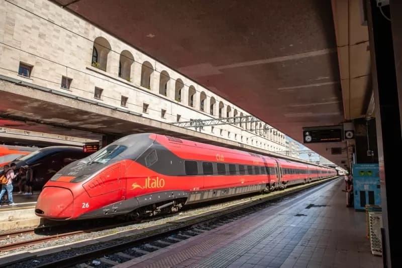A red Italo high speed train waiting at a station platform
