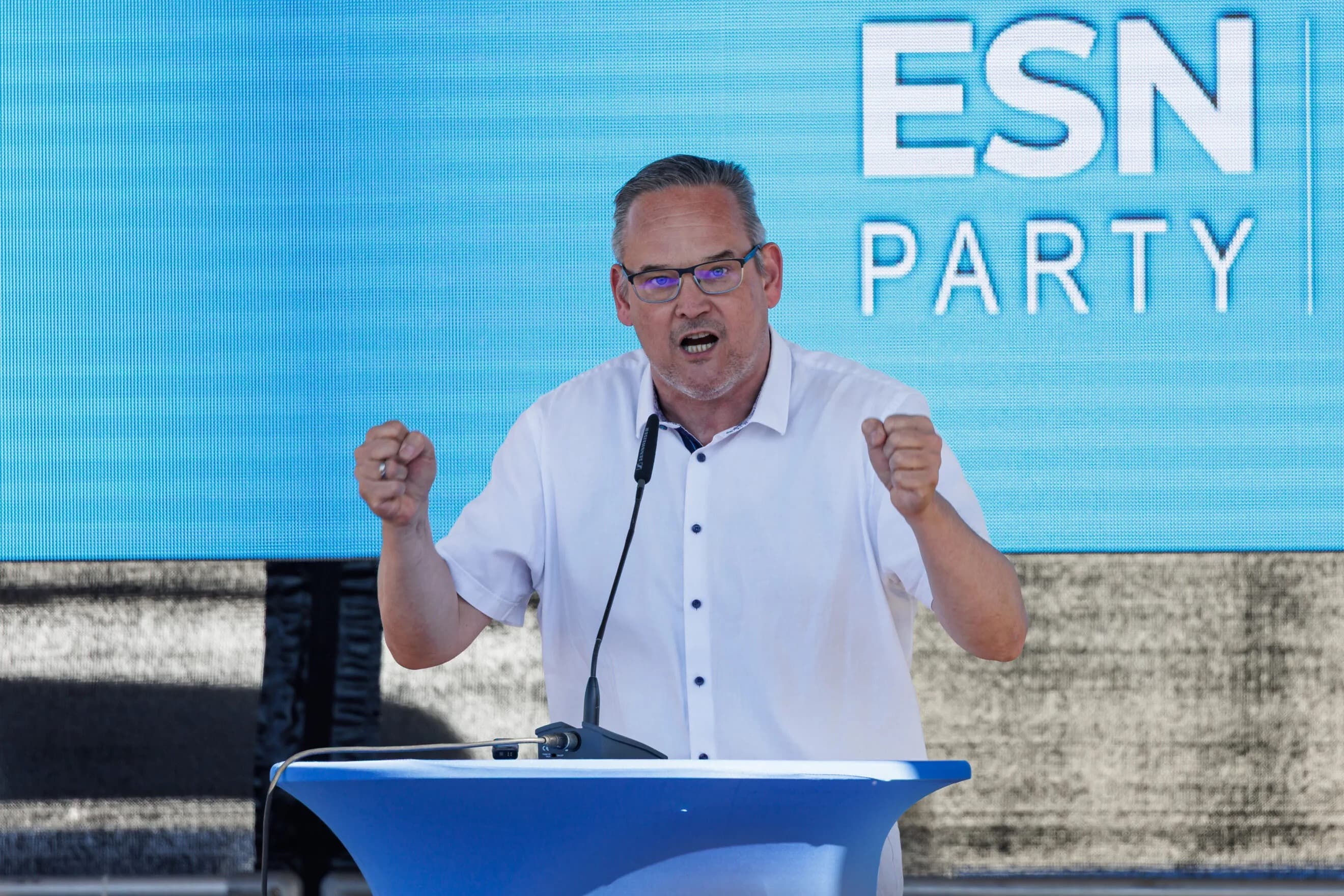 AfD politician Martin Reichardt speaks at a podium in front of a screen reading ESN Party