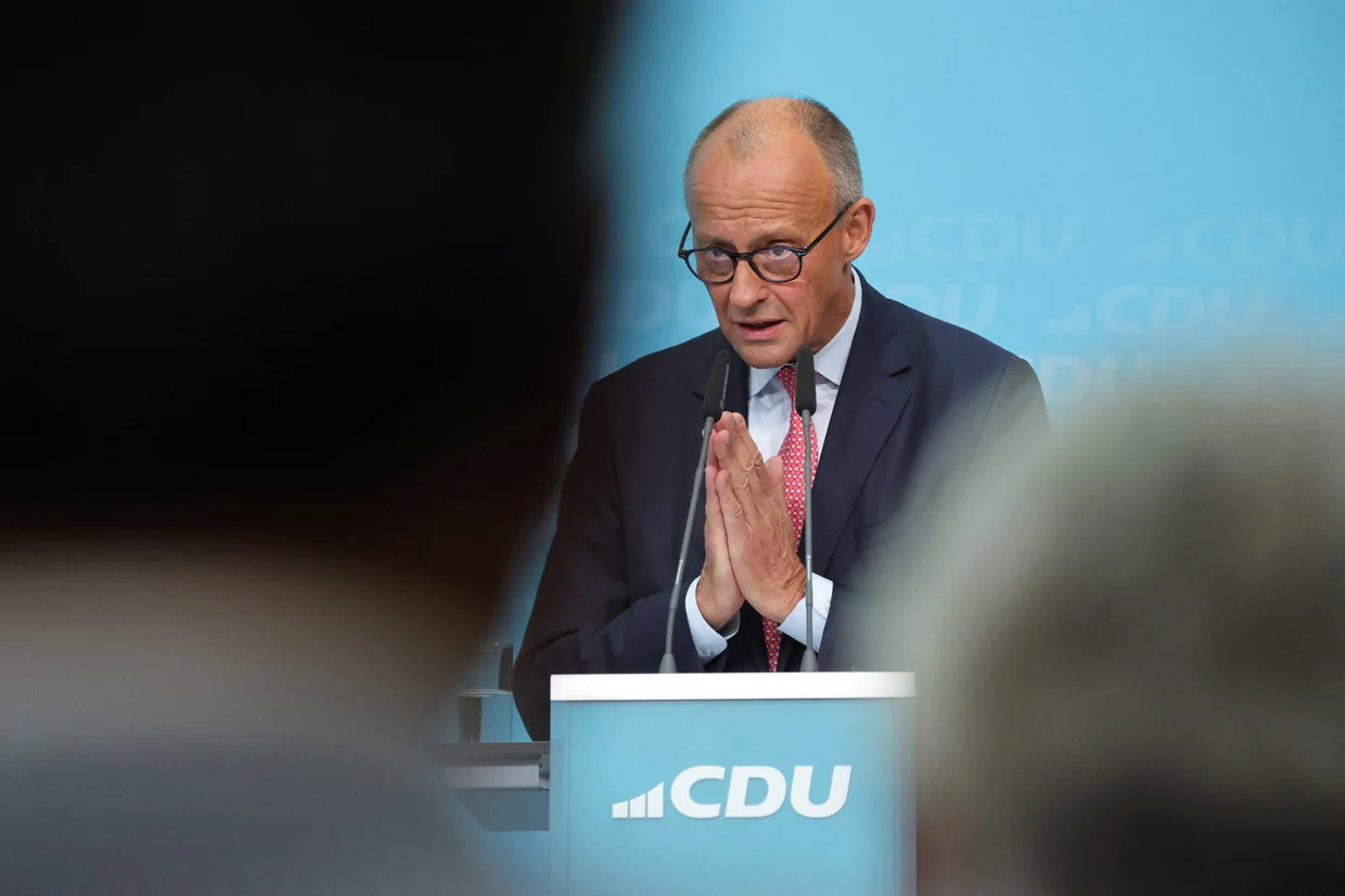 Chancellor Friedrich Merz speaking at a CDU podium as his party faces mounting pressure from the AfD