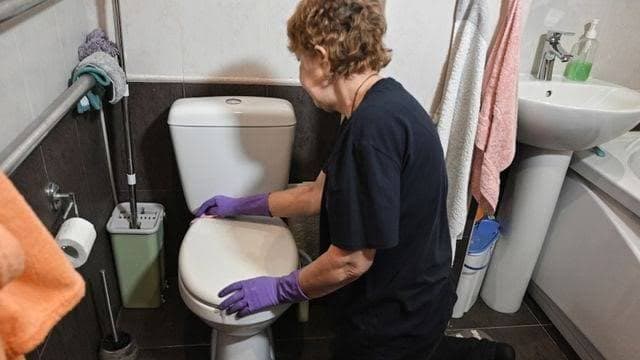 A domestic worker in rubber gloves cleaning a bathroom, a role often held on a minijob contract