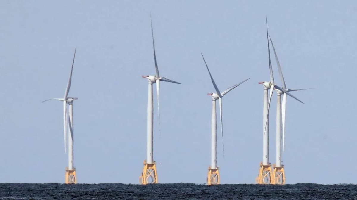 A row of offshore wind turbines standing in the sea against a pale sky