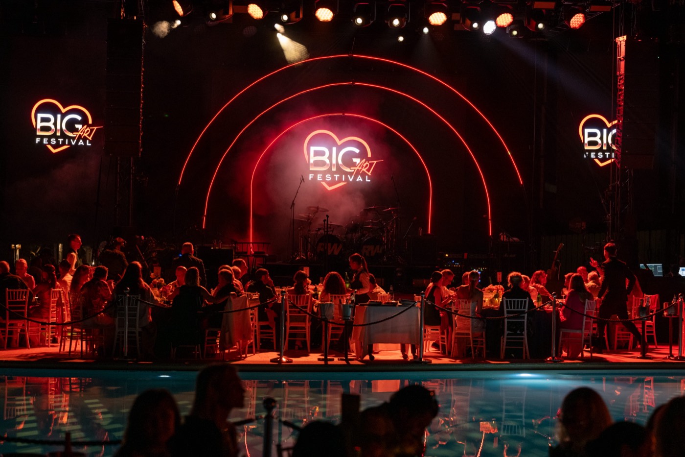 The BIG ART Festival stage lit in red beside the pool at Romazzino, A Belmond Hotel, with guests dining